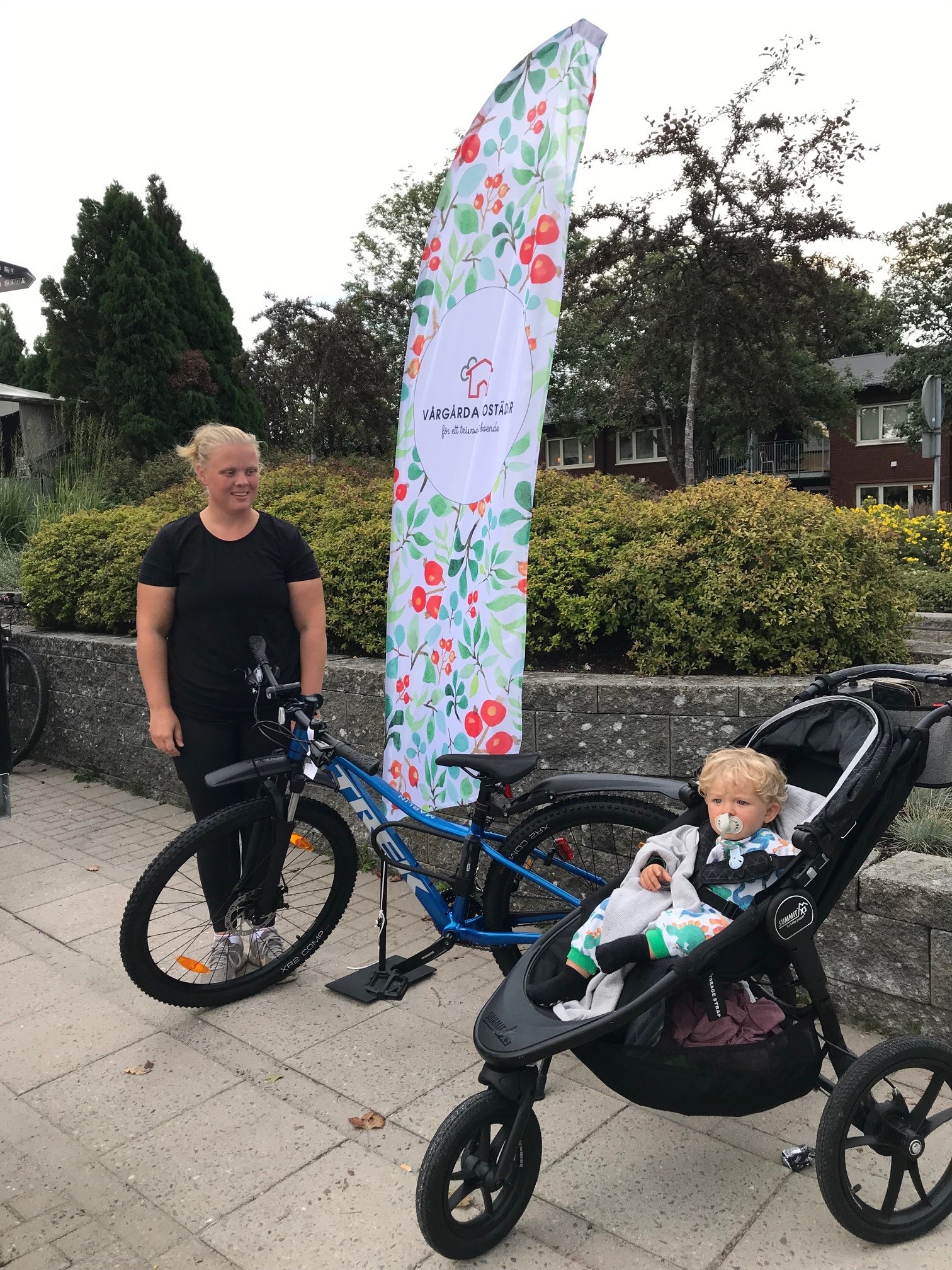 Kvinna med barn i barnvagn står bredvid vunnen cykel
