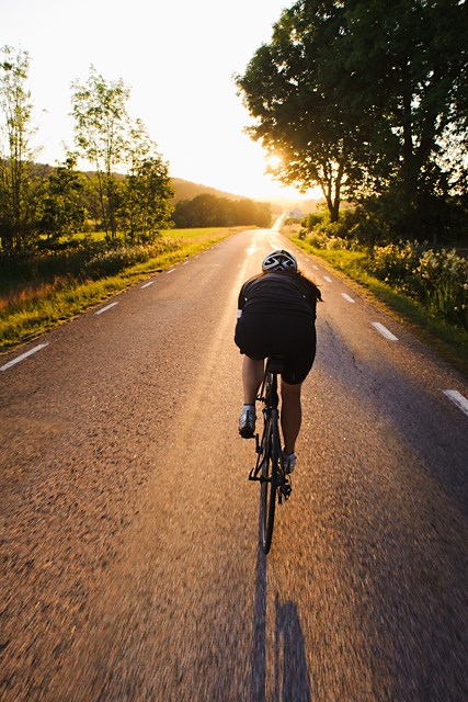 Bild på en man som tävlingscyklar på en landsväg i solnedgången
