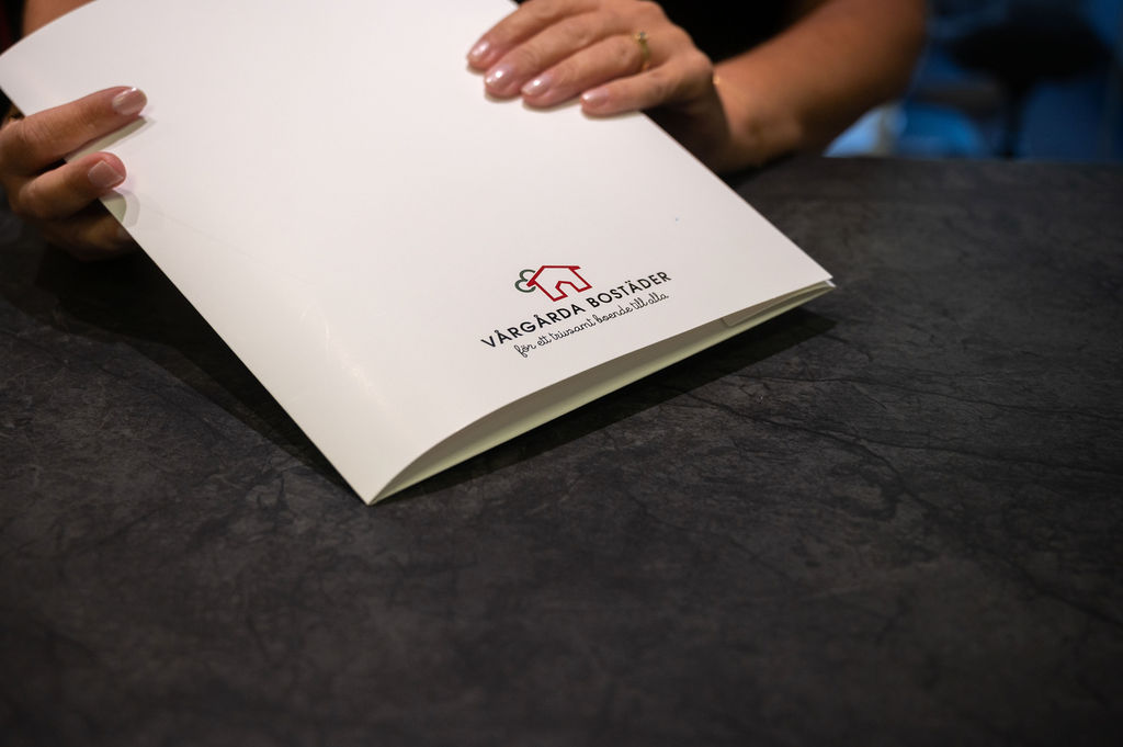 Händer som håller kompendium med Vårgårda Bostäders logga på