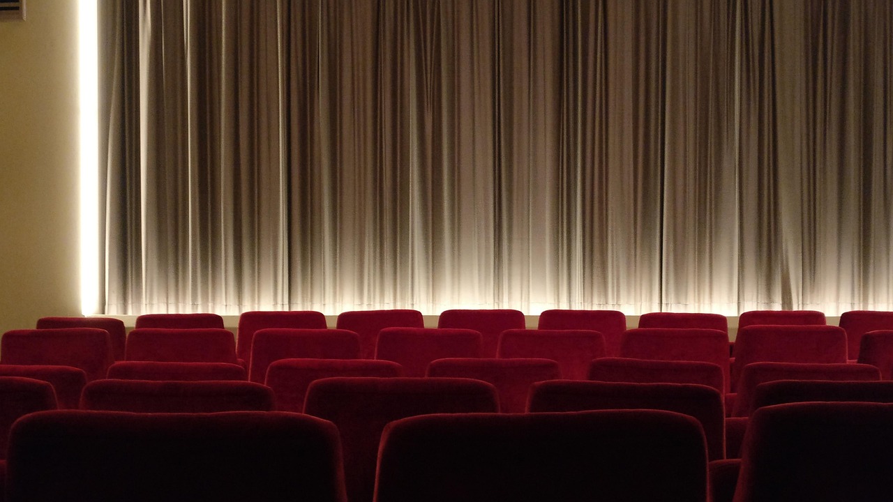 Röda biografstolar i rader vända mot filmduk bakom draperi