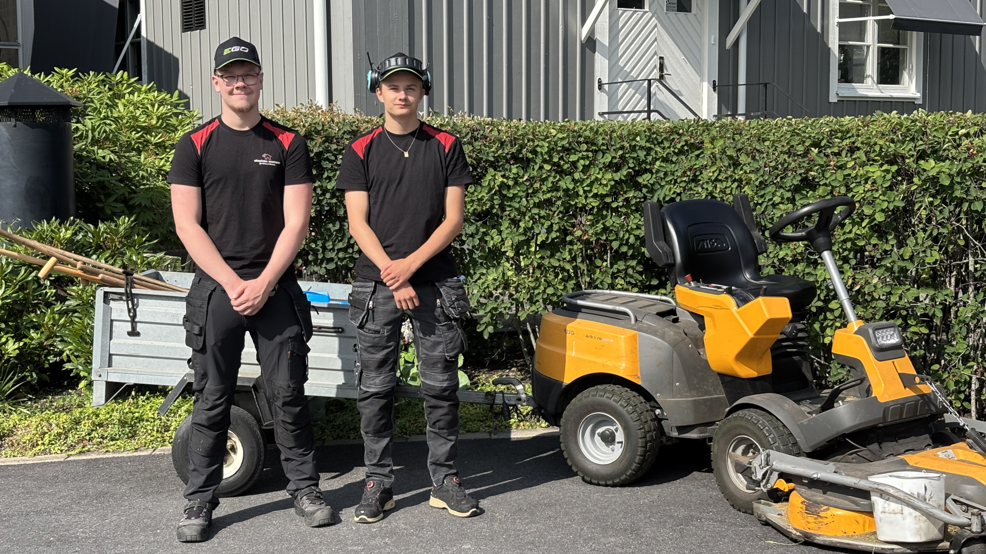 Bild på Neo och Max, sommarjobbare, står framför åkgräsklippare med släp